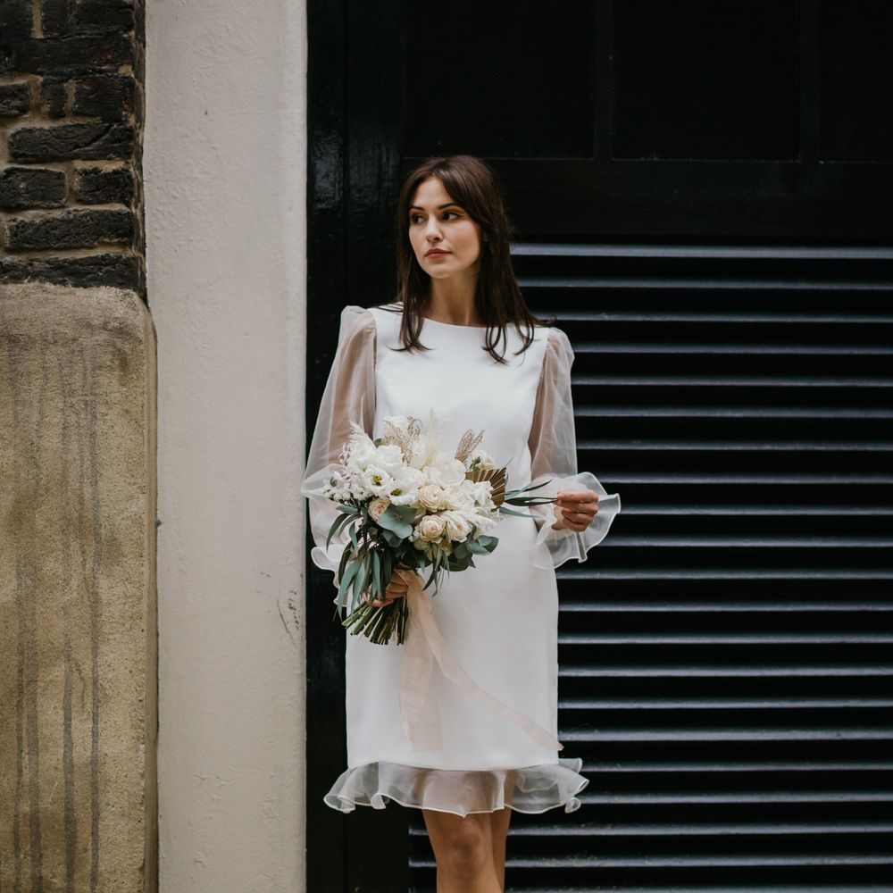 Micro wedding dress by Story Of My Dress with sheer long sleeves and frill edges