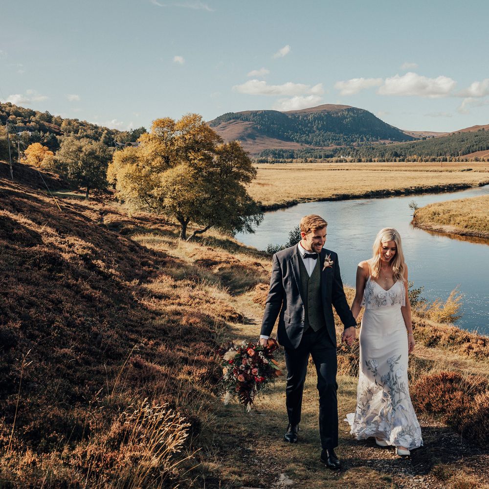 Bride & groom walk through Scottish countryside with lake in the background