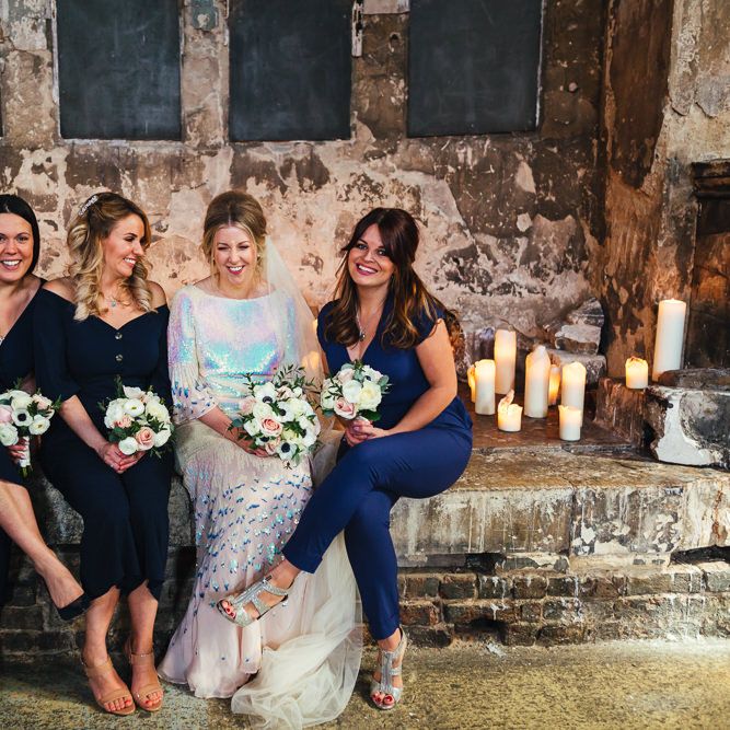 Bride sits with her bridesmaids in different coloured blue jumpsuits