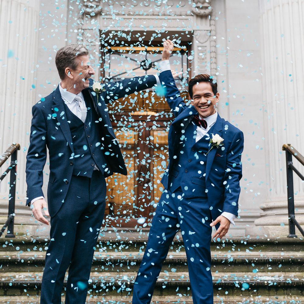 Grooms hold up hands on the steps of the Old Marylebone Town Hall after wedding ceremony