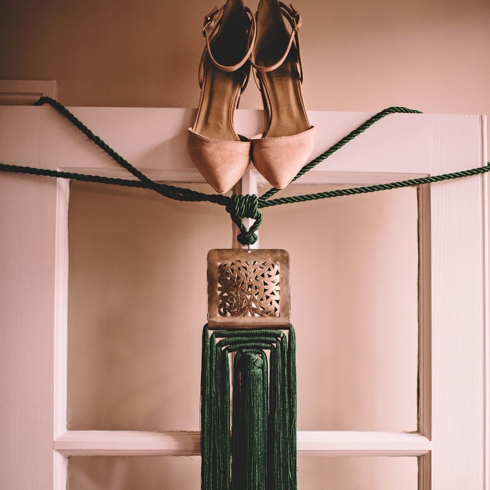 Brides shoes and green clutch bag hang over doorframe on the morning of her wedding day