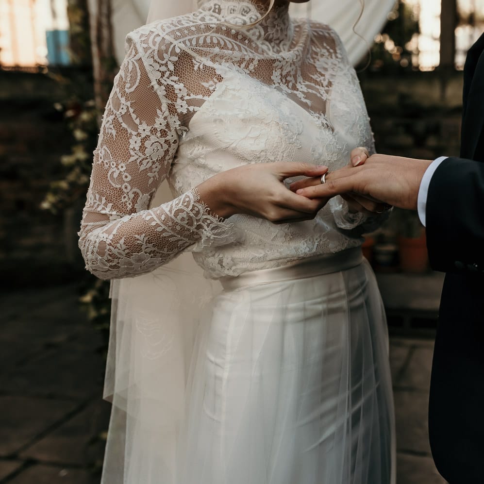 Bride in a long sleeve lace wedding dress putting on her grooms wedding band 