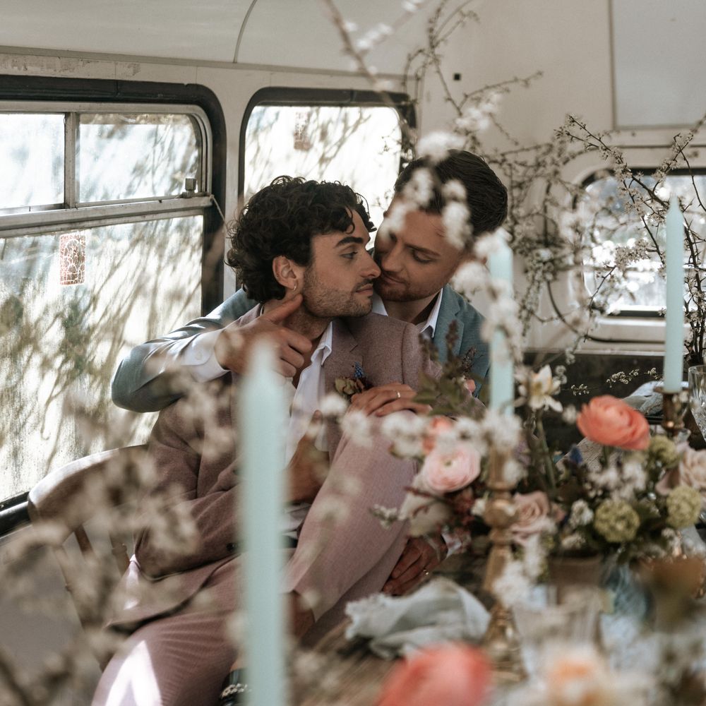 Grooms kiss one another in front of floral bouquets 