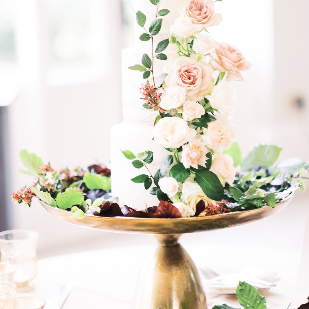 Elegant white iced wedding cake sitting on a gold cake stand with light pink flowers cascading down the front 