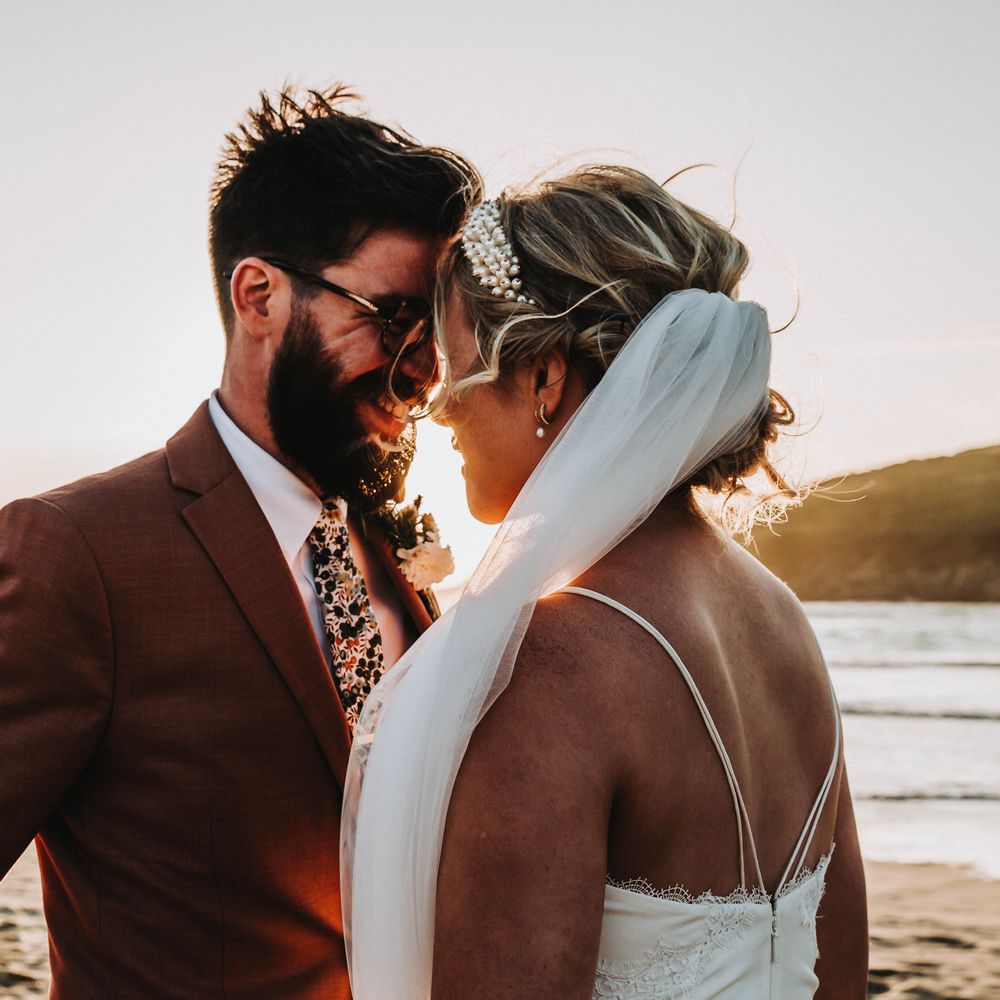 Bride & groom lean in to kiss one another on their wedding day as the sun sets behind them
