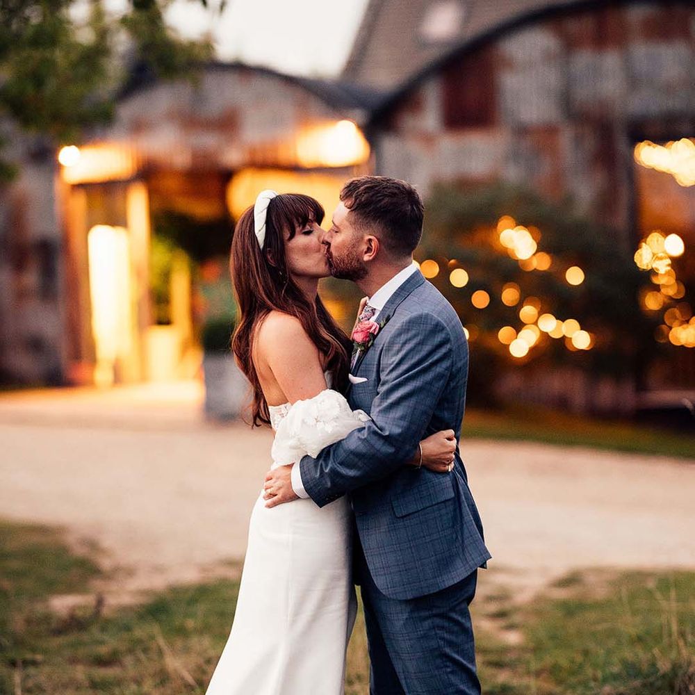 Bride & groom kiss on their wedding day as the sun begins to set at the Stone Barn Cotswolds 