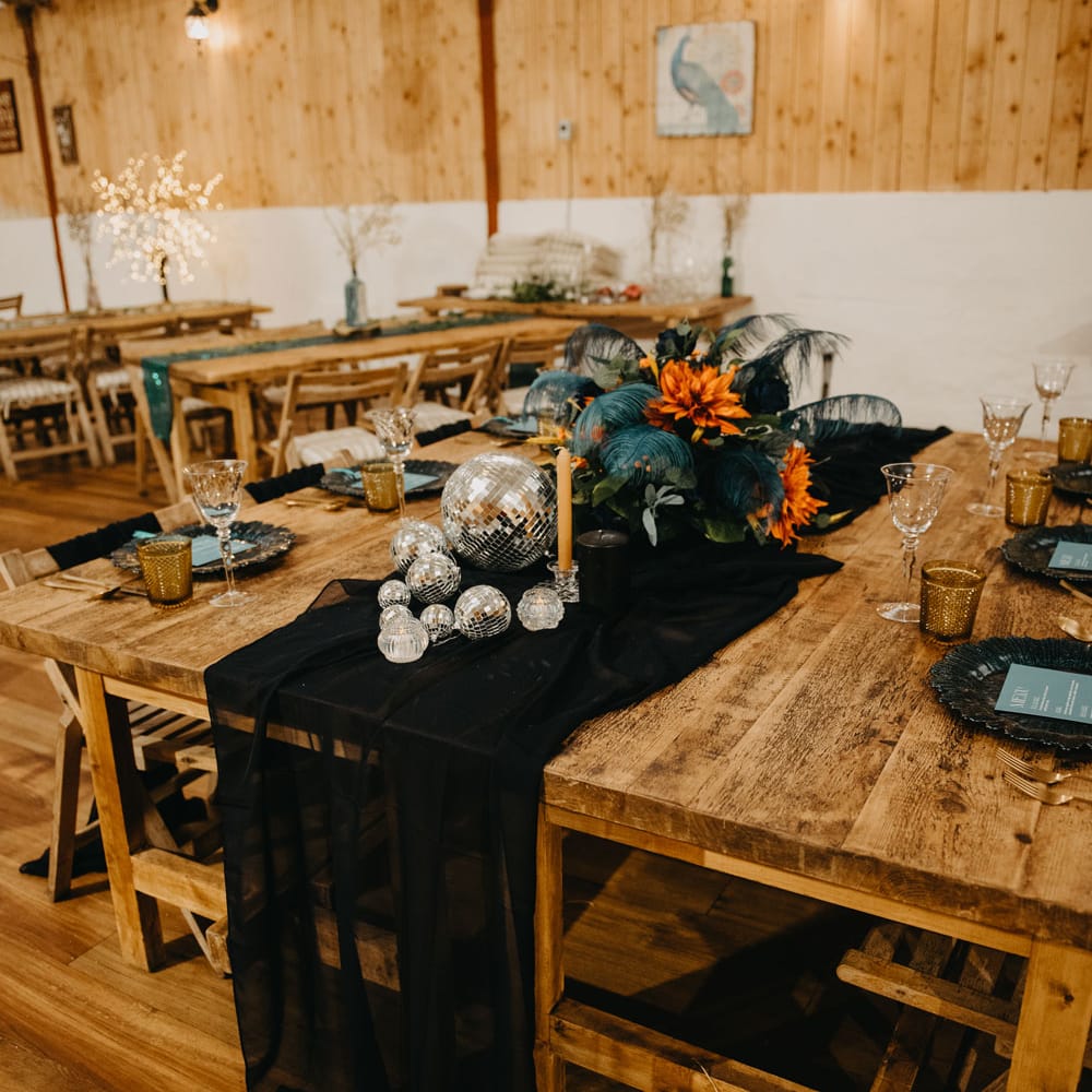 Wooden wedding table with black table runner, disco balls and orange and blue florals for rustic Wellbeing Farm wedding