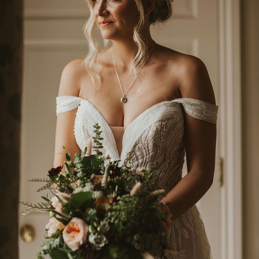 Bride in off the shoulder wedding dress clutches flower bouquet