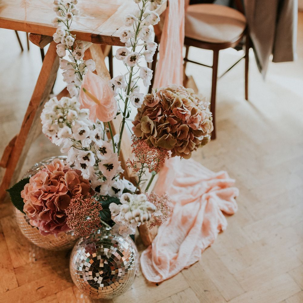 Pale pink floral bouquets complete with disco balls sit on the floor next to table