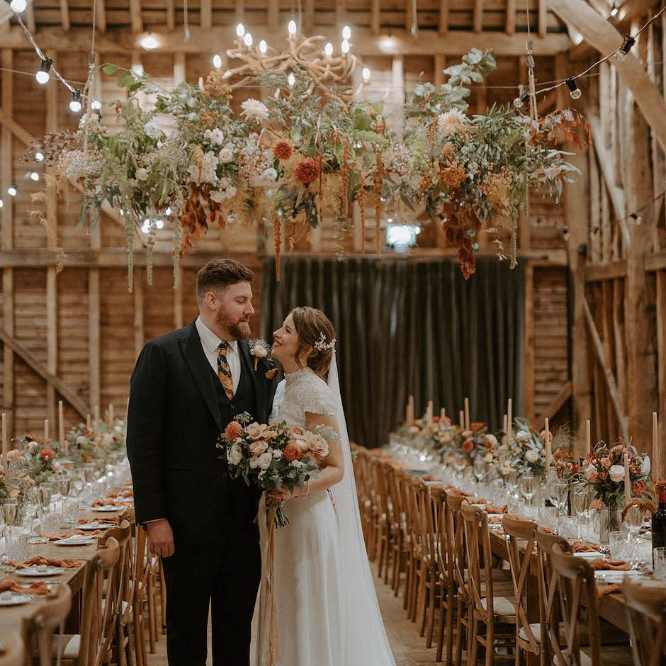 Bride and groom under flower installation at rustic wedding at The Barns at Redcoats