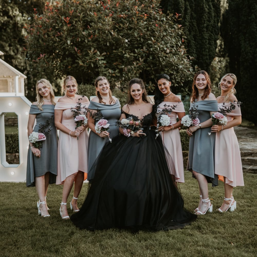 Bride wears black gown and stands with her bridesmaids who wear pink and green pastel bridesmaid gowns