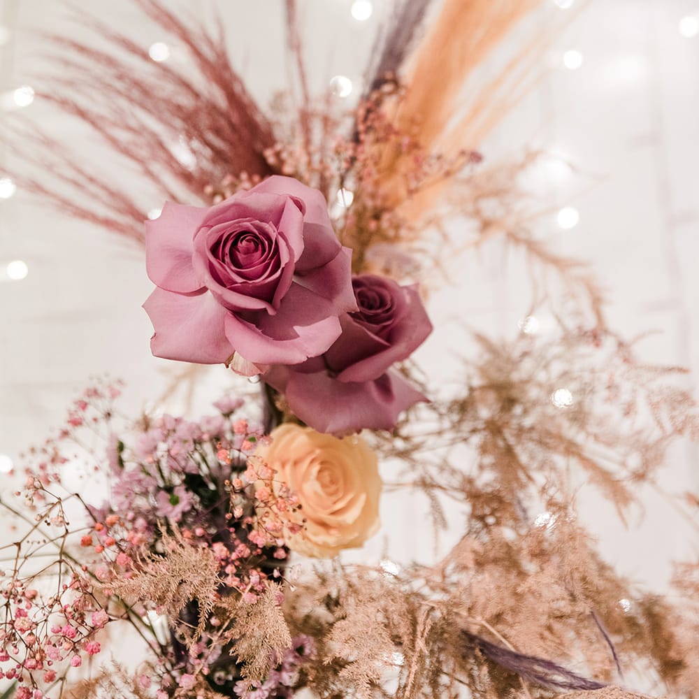 Pink and orange roses with colourful dried grasses in front of fairy light backdrop
