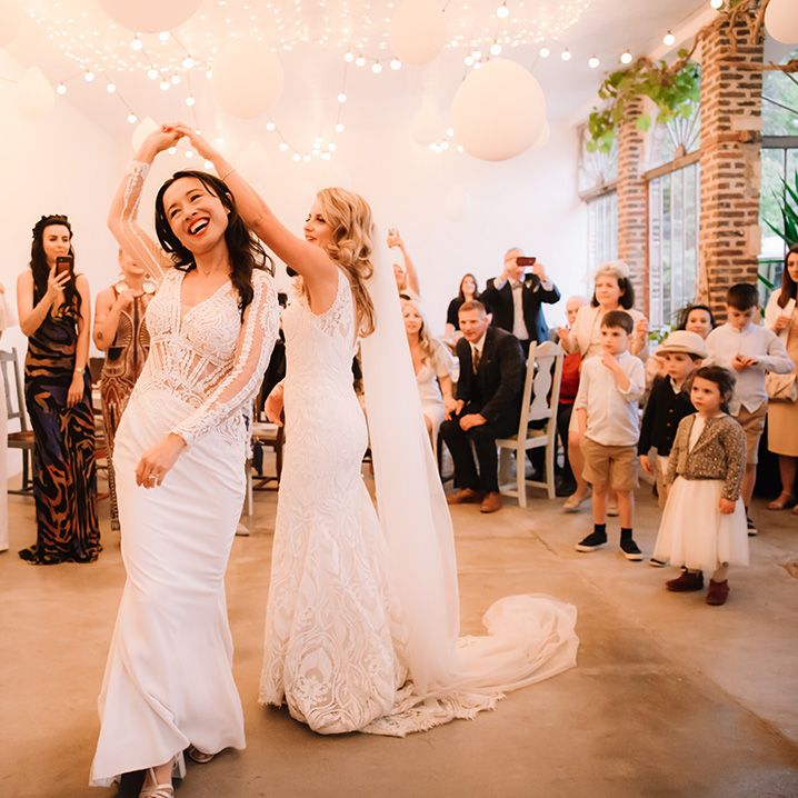 Bride dance together under white balloon and fairy light decoration with guests and children watching on