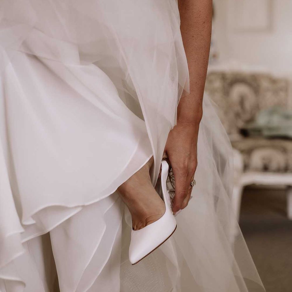 Bride puts on her white pointed butterfly wedding shoes 