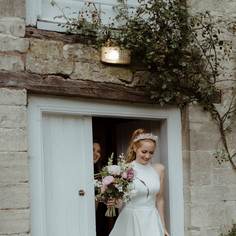 Bride in halter neck wedding dress with pleated skirt and pearl embellished wedding shoes carrying white and pink bouquet 
