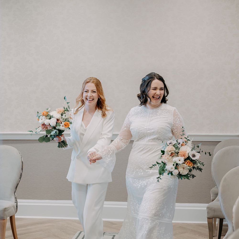 Brides hold hands as they walk with one another on their wedding day
