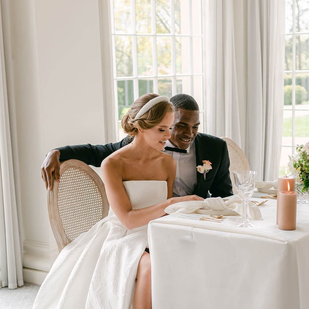 Stylish bride and groom sit together as they look through their wedding menu together 