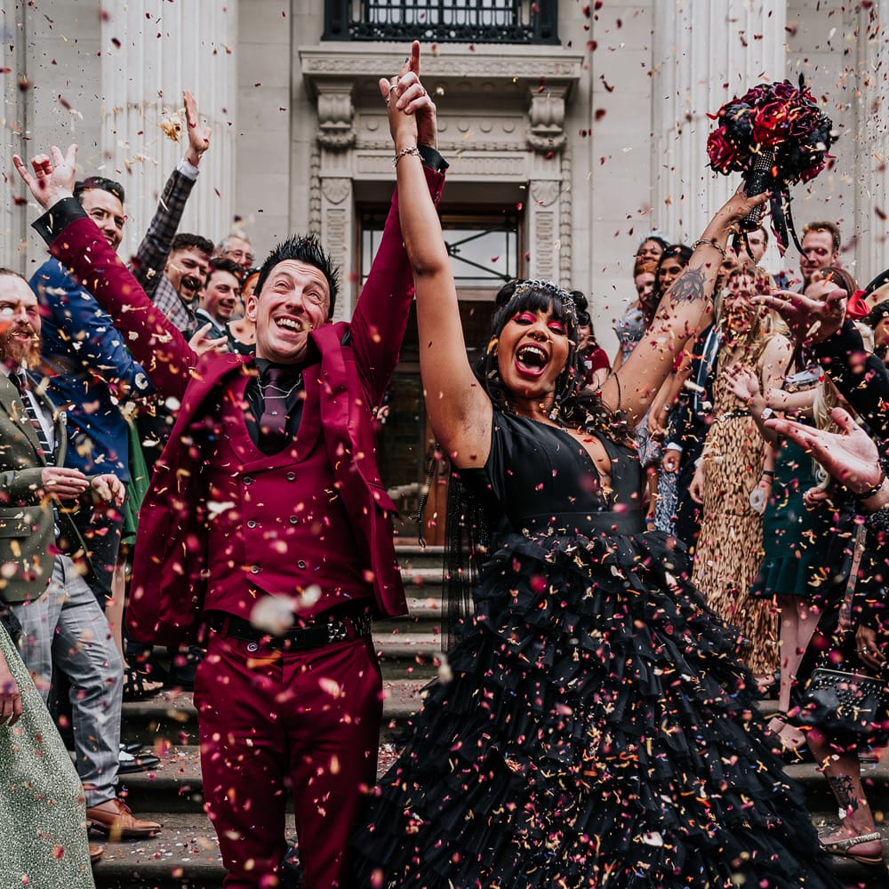 Bride wearing black ruffled wedding dress walks through confetti and celebrates with her groom after Town Hall wedding ceremony