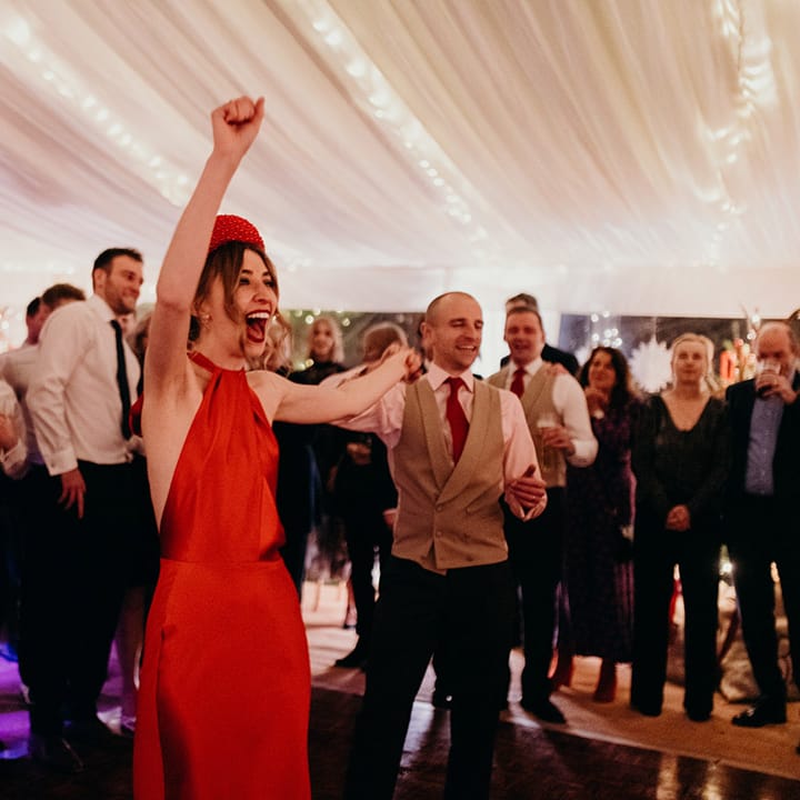 Bride in red silk wedding dress with cape, large red embellished head band and large red satin bow dancing at winter wedding reception