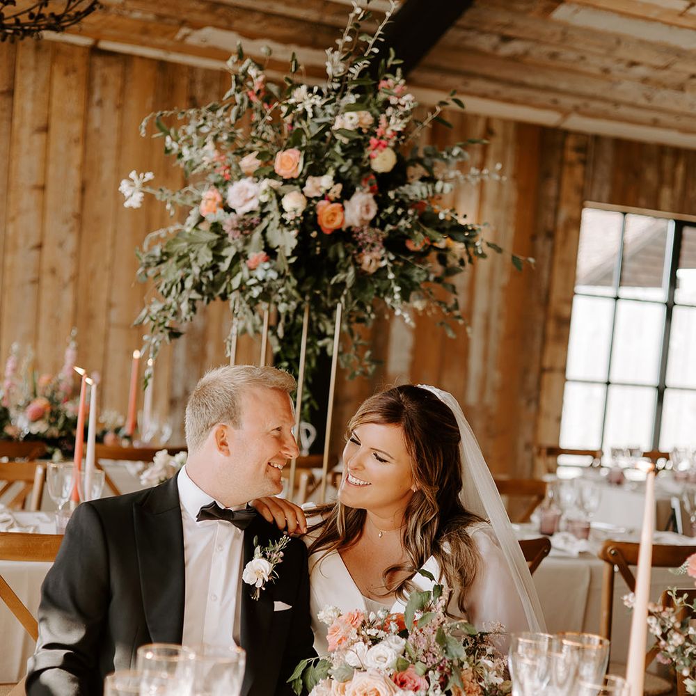 Bride & groom sit in reception surrounded by floral installations with pops of orange 