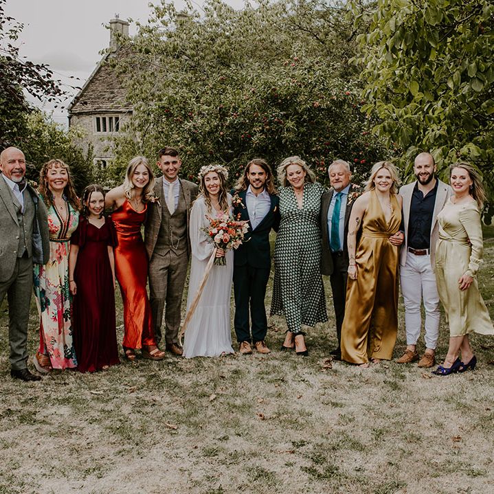 Bride & groom stand with wedding party outdoors with bridesmaids in Autumnal coloured dresses 