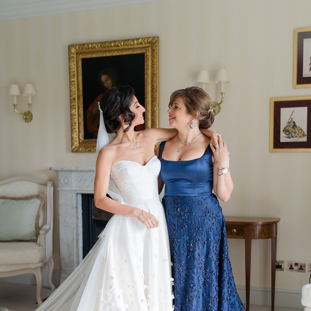 Bride stands with her mother who wears royal blue silk fitted dress with embellished skirt 