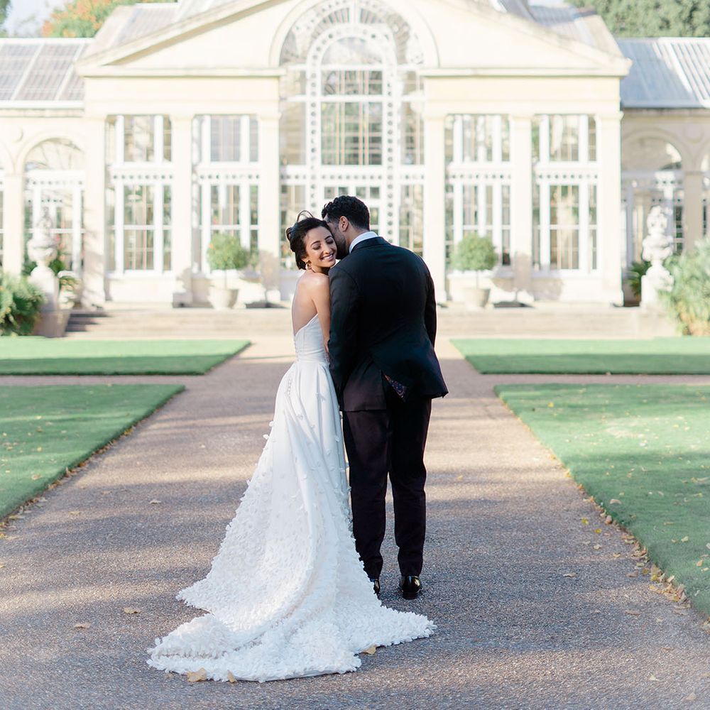 Bride & groom stand in front of Syon Park Conservatory during couples portraits