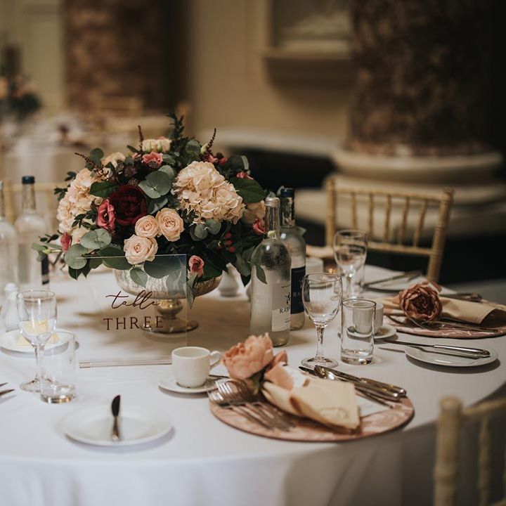 Pink patterned charger plates with pink peonies, a clear acrylic table number sign and arrangement of flowers for the centrepiece 