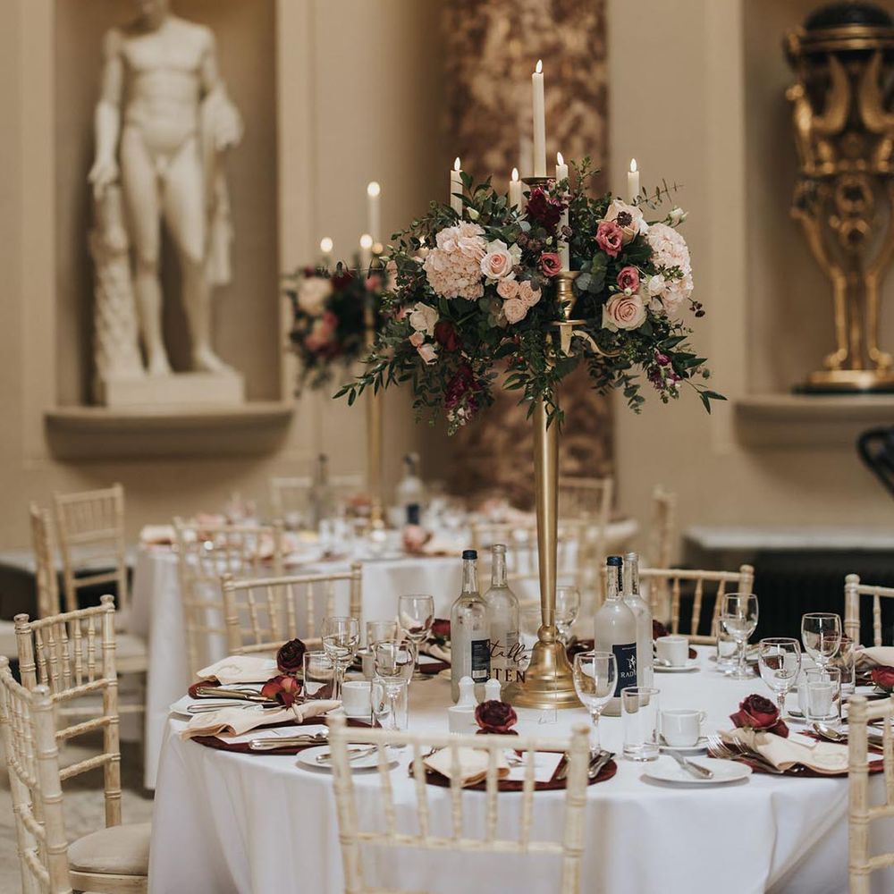Wedding table setting with red place mats and roses and tall flower centrepieces with golden candelabras 