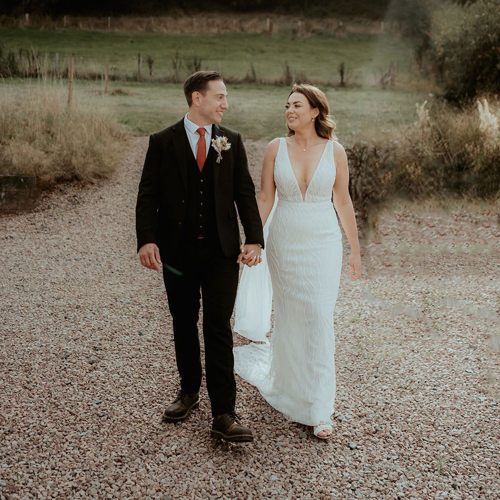 Groom in three piece black suit with a burnt orange tie and dried flower buttonhole with the bride in Made With Love wedding dress 