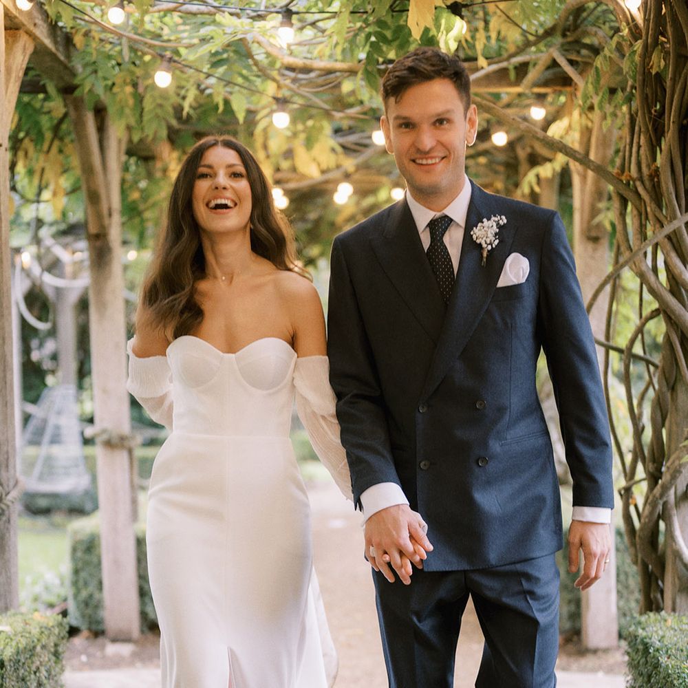 Groom in double breasted navy suit with spotted tie walking hand in hand with the bride in Jimmy Choo pearl shoes and modern wedding dress