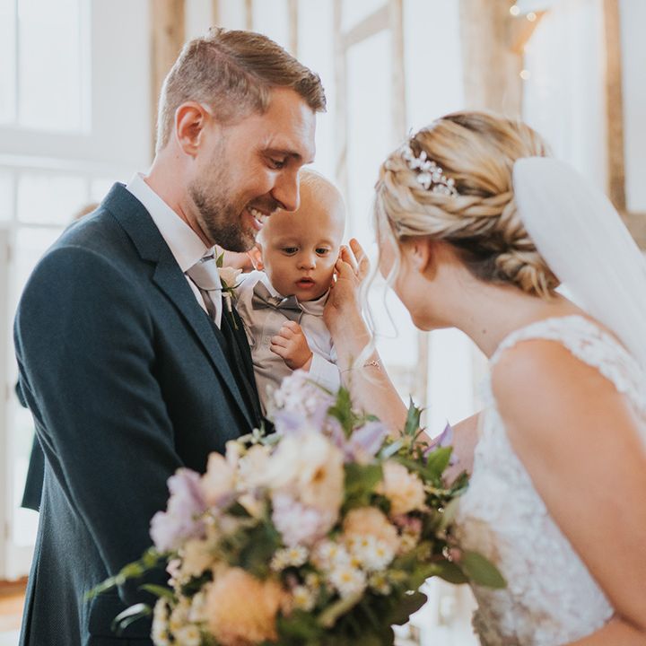 The groom holds his son as they stand at the altar for the wedding ceremony with the bride showing their son some love 