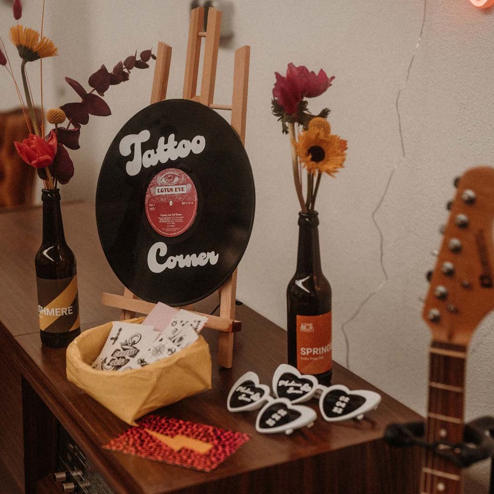 Vinyl wedding decor - flash temporary tattoos for wedding on wooden table with orange and pink wedding flower arrangements in beer bottles, leopard print wedding stationery and white heart shaped wedding sunglasses 