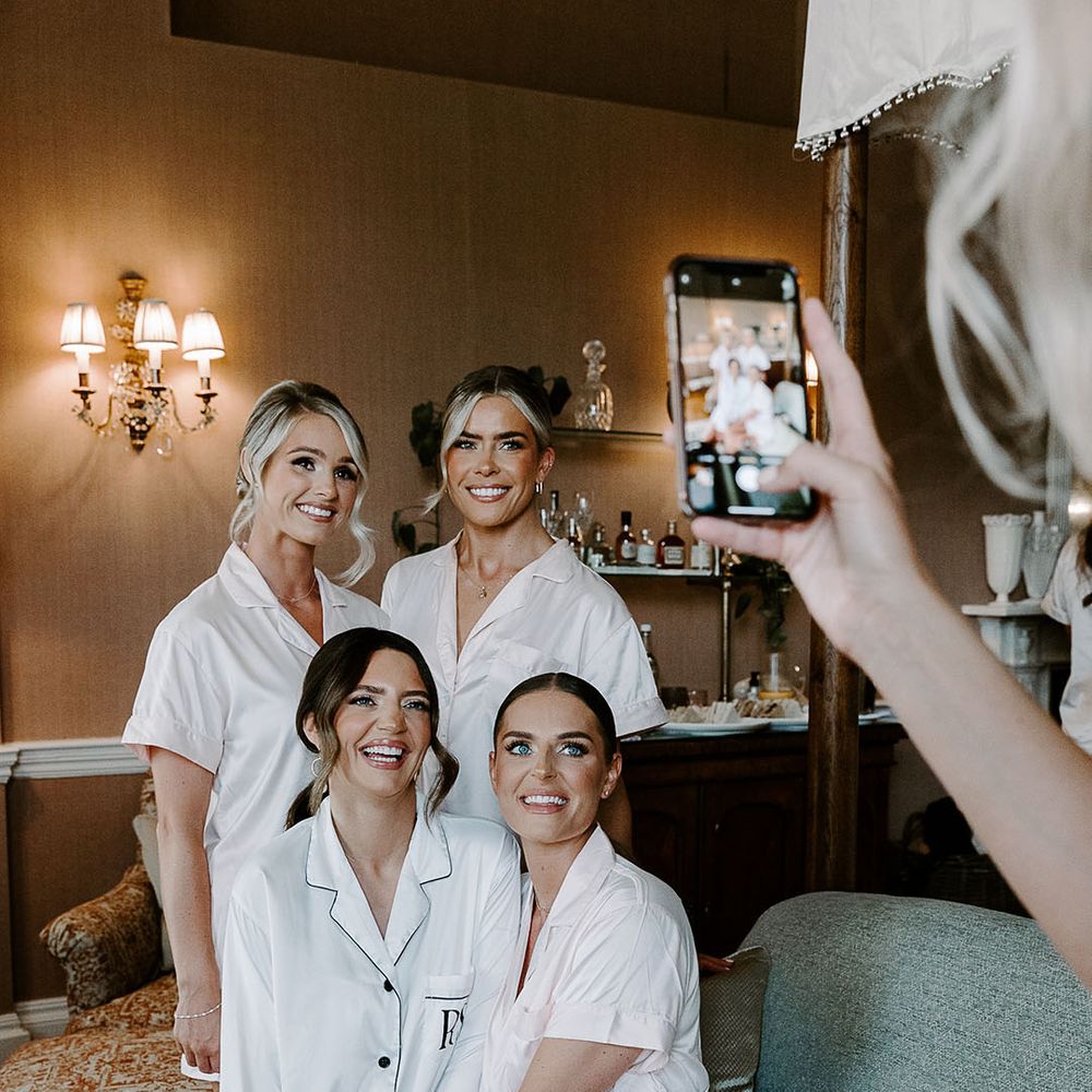 Bride and bridesmaids in white satin pyjamas getting ready in the morning together 