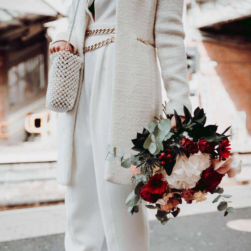 Bride in Massimo Dutti jumpsuit with red shoes and red, white and foliage bouquet 
