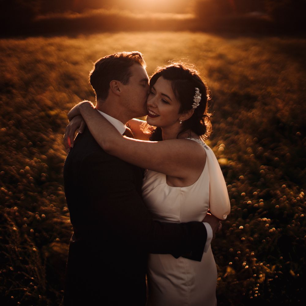 Bride & groom embrace during golden hour with sun setting
