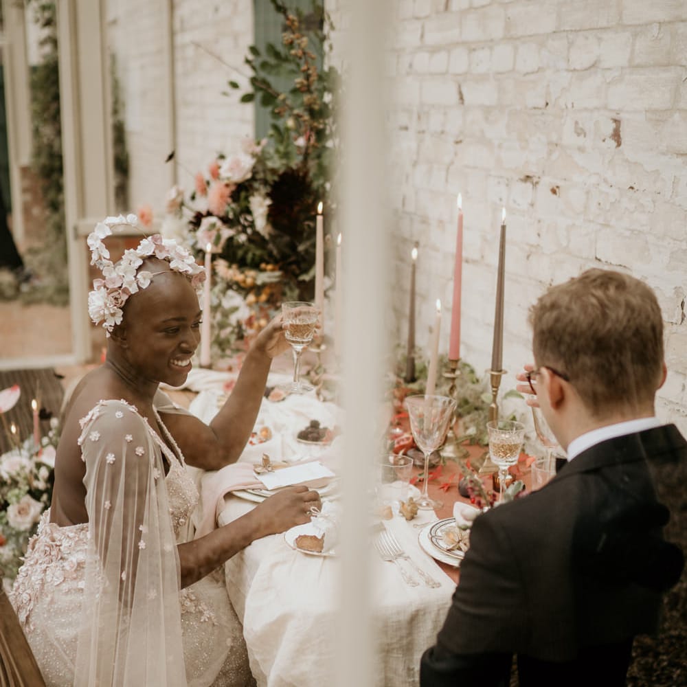 Bride with alopecia sitting at her intimate elopement reception in an embellished blush pink wedding dress with watteau train and floral headdress 
