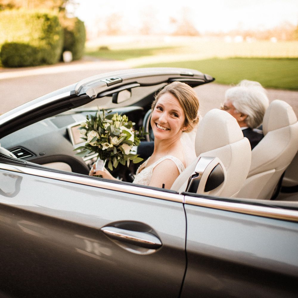 Bride sits in car with veil blowing in the wind