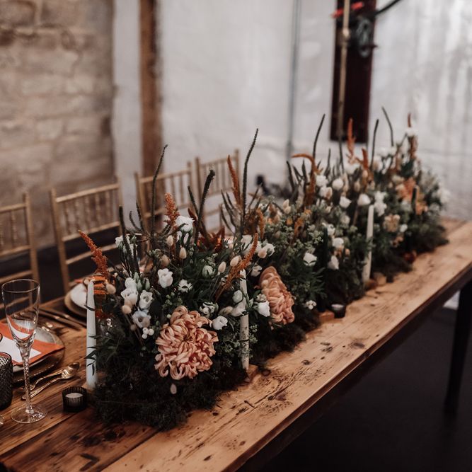 Orange and white flowers mixed with foliage and candles for wedding reception decor 