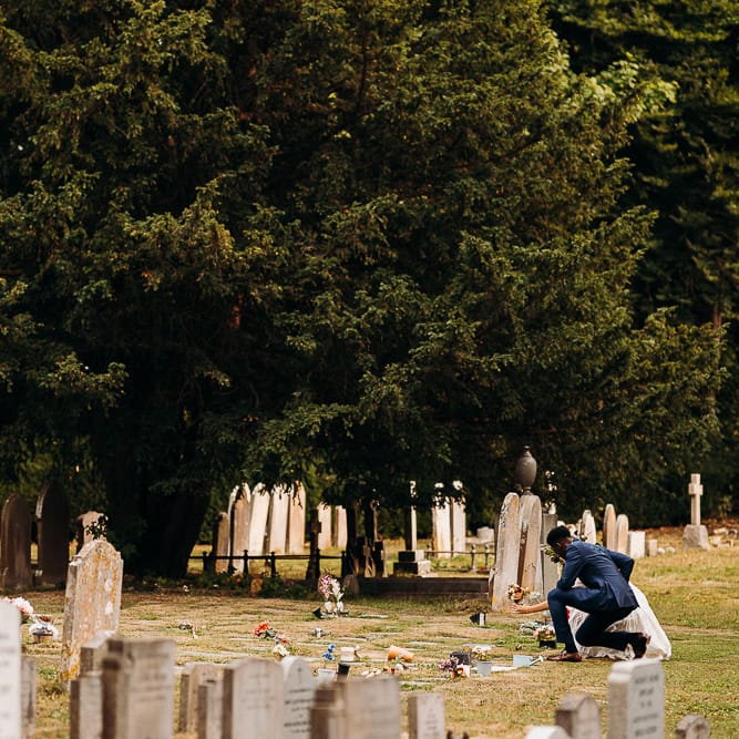 Bride and groom laying flowers on a grave at their church wedding 