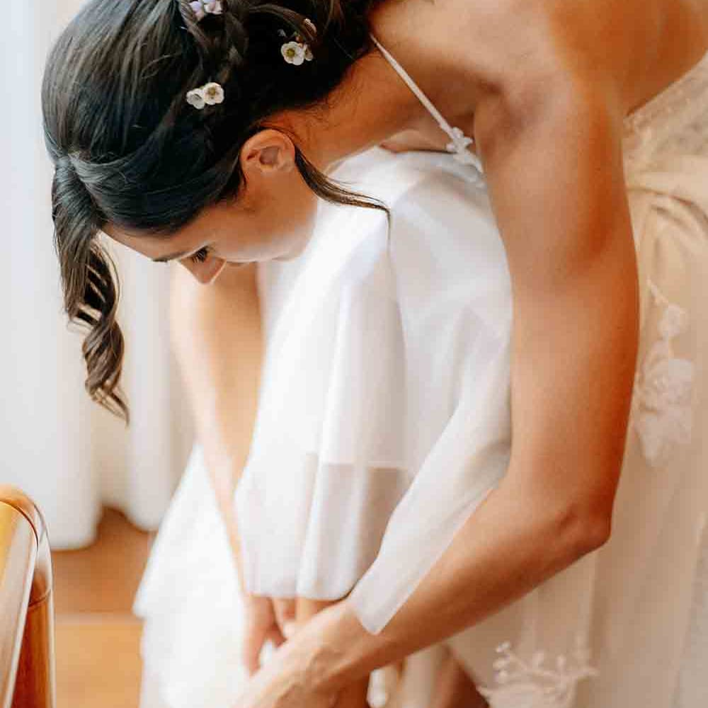 Bride fastens her white wedding shoes for Italian wedding