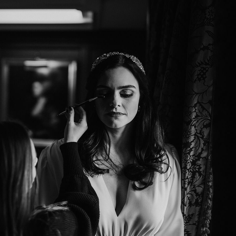 Black and white wedding day photography of bride applying wedding day makeup