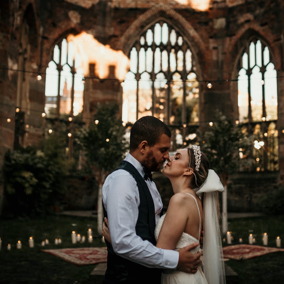 Stylish bride and groom kissing in an open air church with festoon light decor 