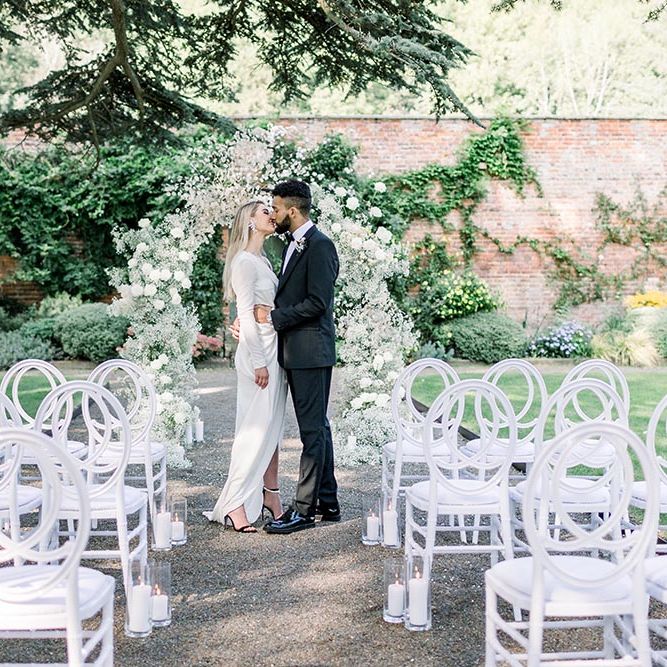 Bride and groom kissing in front of a white floral arch at Garthmyl Hall wedding venue 