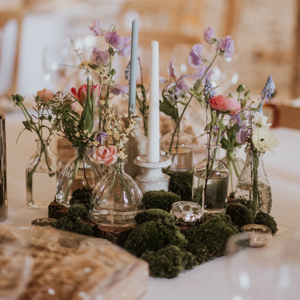 Moss centrepiece decor with ink wells and small vases filled with colourful flowers and taper candles 
