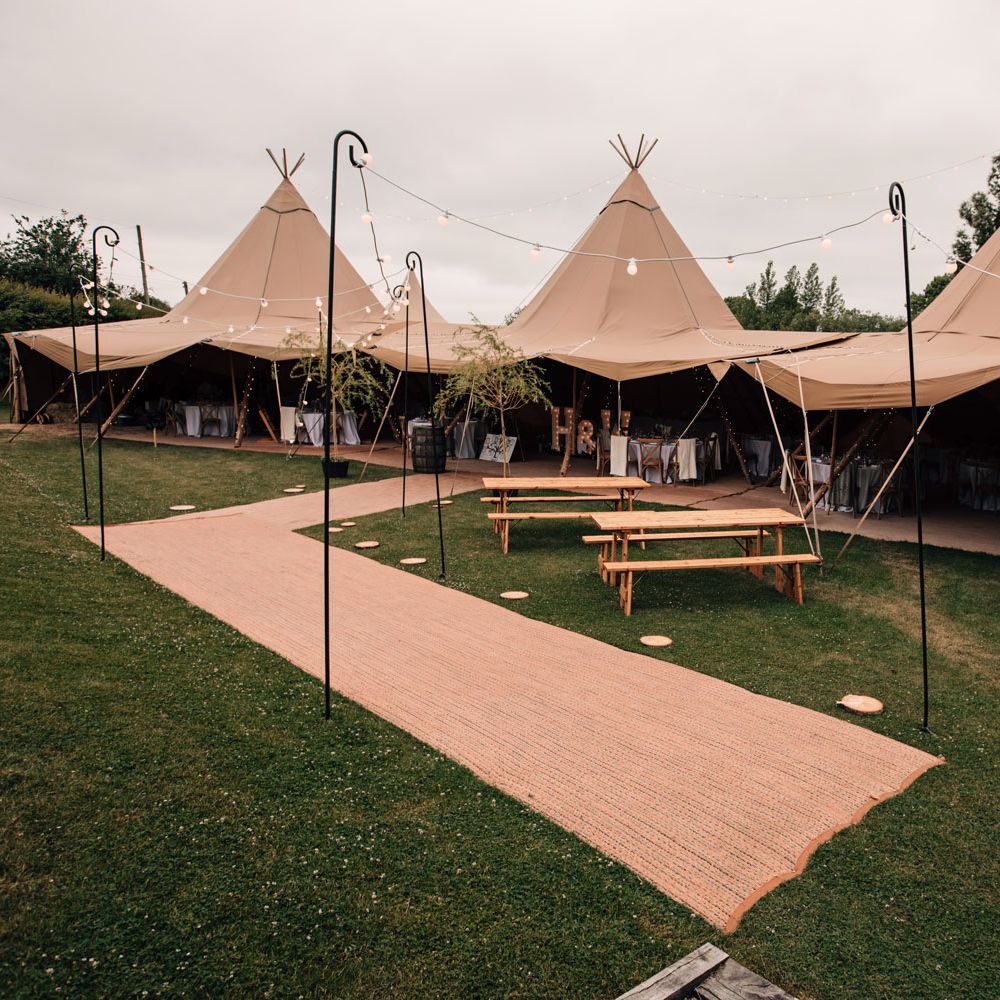 Large garden wedding tipi with wooden benches and shepherds hook lights for rustic wedding reception