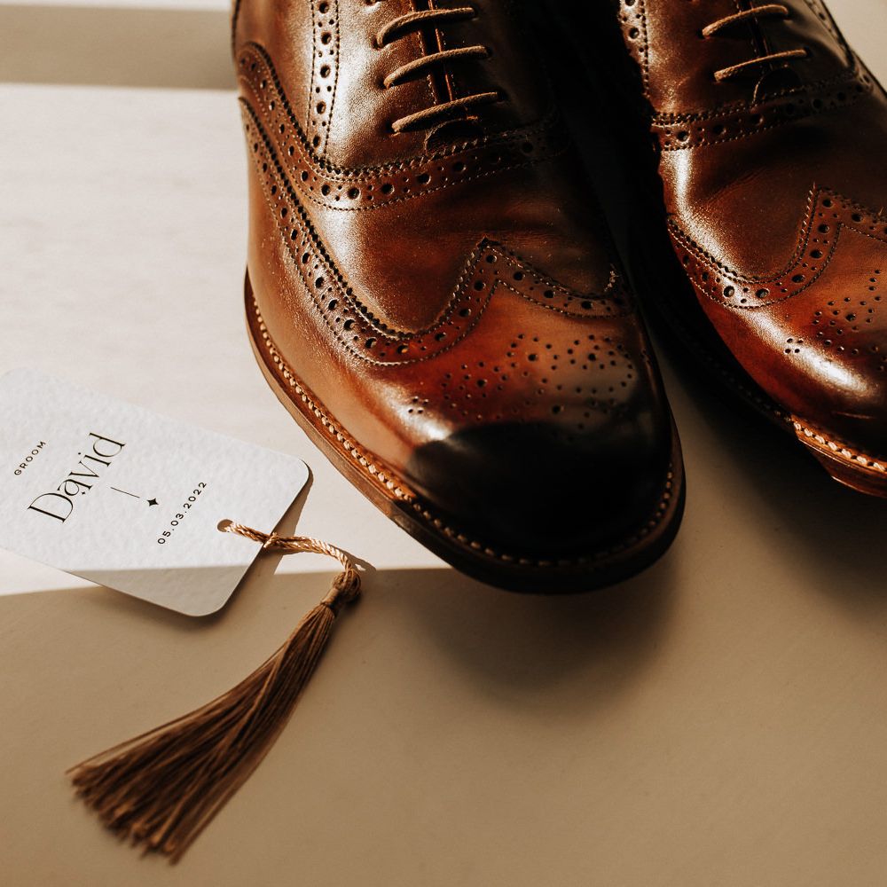 Brown brogues next to white table place name with monochrome typography and brown tassel 