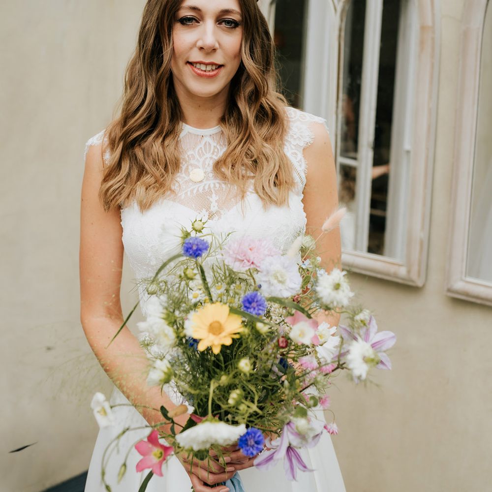 Bride with wavy braided hair and lacy wedding top holding colourful wildflower wedding bouquet