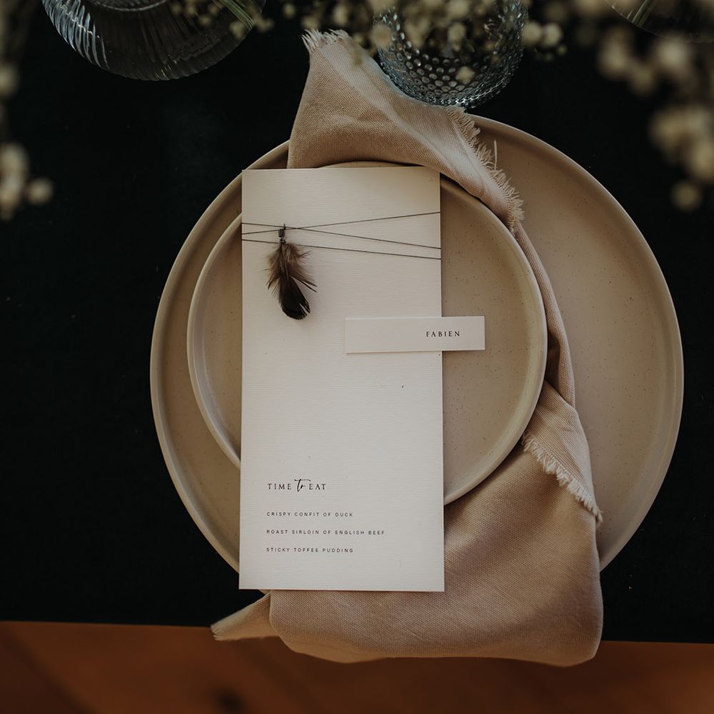 Place setting with beige plates and menu card with feather detail 