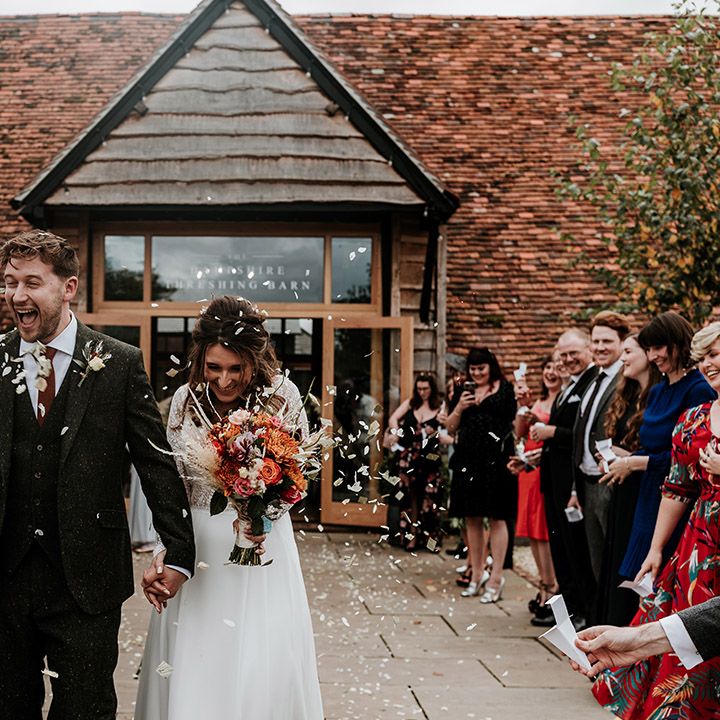 Smiling bride and groom have their confetti exit after ceremony with groom in wool green suit and bride in illusion lace long sleeve wedding dress